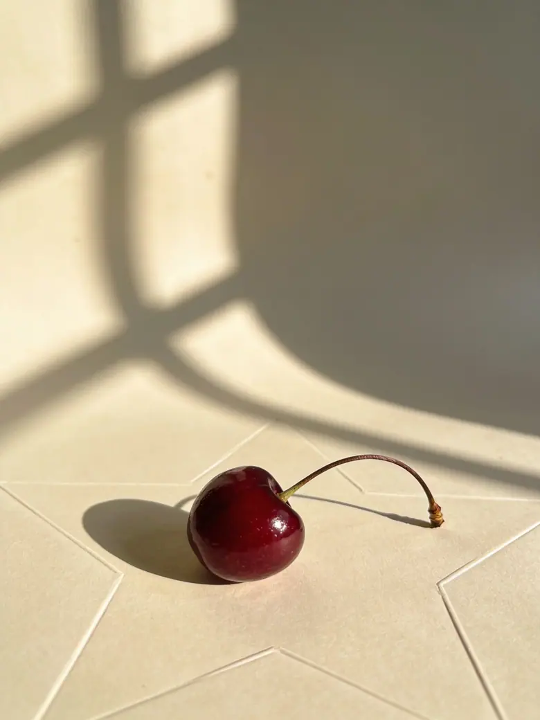 A single cherry on cream paper in raking sunlight